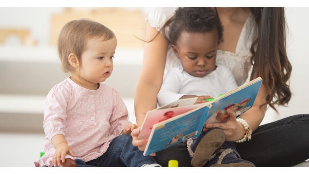 A caregiver reading a picture book with two toddlers